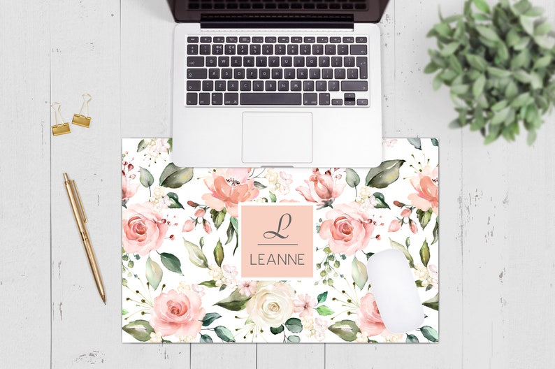 May include: A pink and white floral desk mat with a personalised name, "LEANNE", in a pink square with a cursive "L" above it.