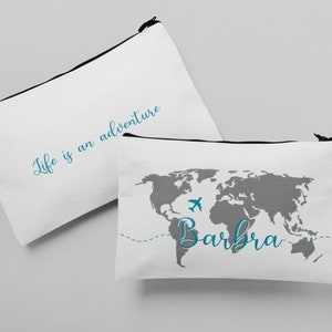 May include: Two white zippered pouches. One pouch has the text "Life is an adventure" in blue cursive. The other pouch has a gray world map with a blue airplane and the name "Barbra" in blue cursive.