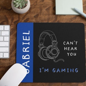 May include: A blue and black gaming mouse pad with the text "I'm Gaming" and "Can't Hear You" with a drawing of headphones. The left side of the mouse pad has the name "Gabriel" written vertically in white.