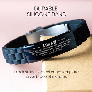 Op de afbeelding: Zwarte siliconen armband met een gegraveerde plaat van zwart roestvrij staal en zilveren armbandsluitingen. Op de plaat staat "LOGAN" en een persoonlijke boodschap. De tekst "DURABLE SILICONE BAND" staat bovenaan.