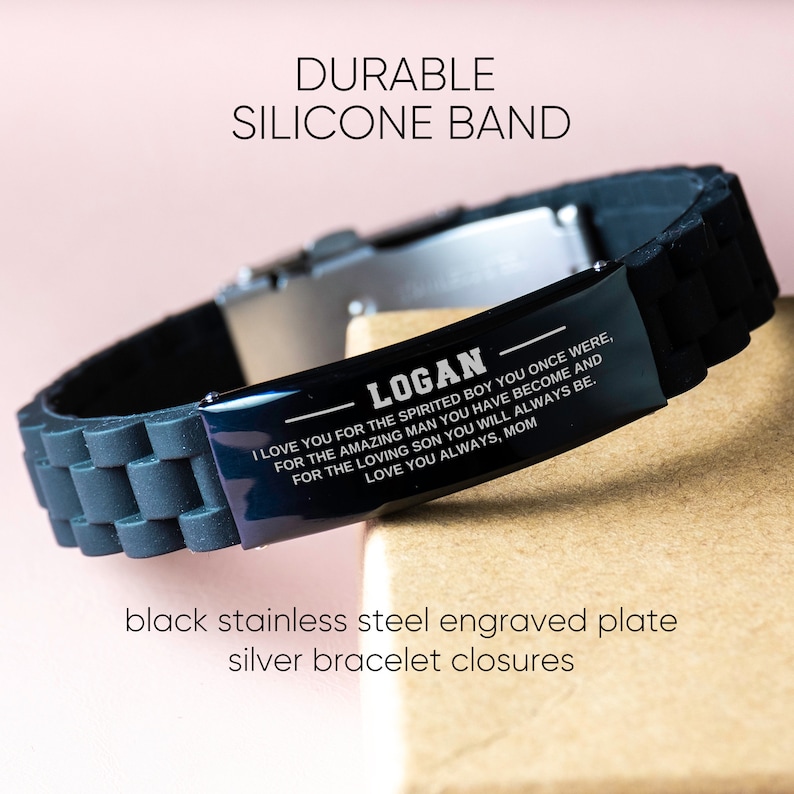 Op de afbeelding: Zwarte siliconen armband met een gegraveerde plaat van zwart roestvrij staal en zilveren armbandsluitingen. Op de plaat staat "LOGAN" en een persoonlijke boodschap. De tekst "DURABLE SILICONE BAND" staat bovenaan.