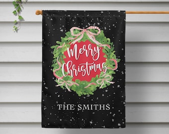 May include: Black Christmas garden flag with a wreath design. The wreath features green leaves, pink bows, and a red center with "Merry Christmas" in white script. The family name "THE SMITHS" is printed at the bottom.