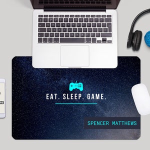 May include: A black and blue gaming mouse pad with a starry night sky design. The text "EAT. SLEEP. GAME." is printed in white with a blue line underneath. The text "SPENCER MATTHEWS" is printed in blue at the bottom of the mouse pad.