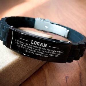 Op de afbeelding: Zwarte siliconen armband met een roestvrijstalen sluiting. De zwarte metalen plaat is gegraveerd met de naam "LOGAN" en een liefdevolle boodschap van "MOM".