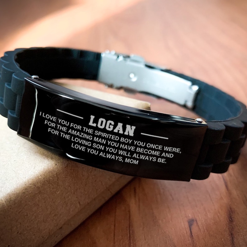 Op de afbeelding: Zwarte siliconen armband met een roestvrijstalen sluiting. De zwarte metalen plaat is gegraveerd met de naam "LOGAN" en een liefdevolle boodschap van "MOM".