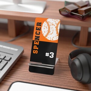May include: Black and orange phone stand with a baseball graphic and the text "SPENCER #3".