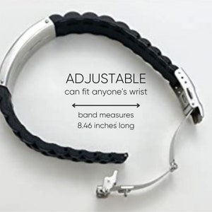Op de afbeelding: Zwarte en zilveren horlogeband met de tekst "ADJUSTABLE can fit anyone's wrist". De band meet 21,49 cm lang. De band is gemaakt van zwart rubber en zilverkleurig metaal.