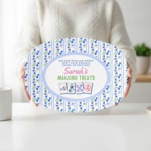 May include: An oval serving tray with a white background featuring a repeating pattern of blue and green mahjong tiles. The center has a light blue oval border with the text: BECAUSE REGULAR GAMES DON'T HAVE ENOUGH DRAMA OR DRAGONS, Sarah's MAHJONG TREATS.