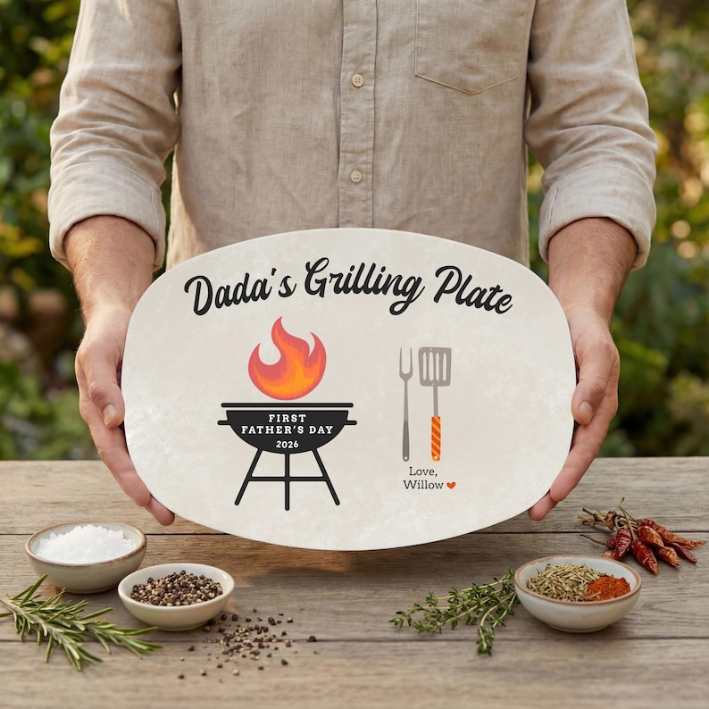 May include: An oval grilling plate with the text "Dada's Grilling Plate" and a grill graphic. The plate also features a flame, a spatula, and the text "First Father's Day 2026". The plate is held by a person.