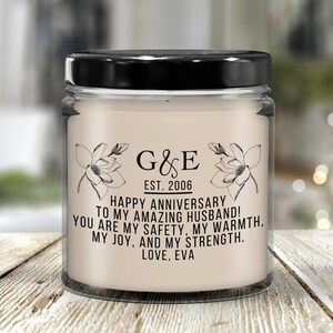 May include: A white candle with a black lid and a label that reads "G&E EST. 2006" and "HAPPY ANNIVERSARY TO MY AMAZING HUSBAND! YOU ARE MY SAFETY, MY WARMTH, MY JOY, AND MY STRENGTH. LOVE, EVA."