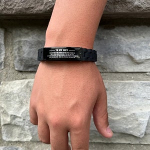 Op de afbeelding: Zwarte siliconen armband met een rechthoekige metalen plaat. De plaat heeft de tekst "TO MY MVP" en een langere boodschap eronder. De armband wordt om een pols gedragen.