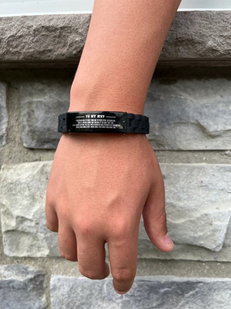 Op de afbeelding: Zwarte siliconen armband met een rechthoekige metalen plaat. De plaat heeft de tekst "TO MY MVP" en een langere boodschap eronder. De armband wordt om een pols gedragen.
