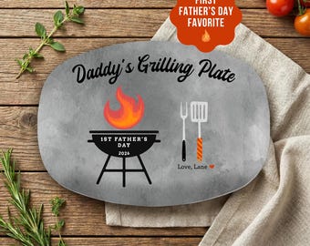 May include: An oval gray plate with the text Daddy's Grilling Plate, a graphic of a black grill with a flame, the text 1ST FATHER'S DAY 2026, a fork and spatula illustration, and the text Love, Lane with a small red heart symbol.