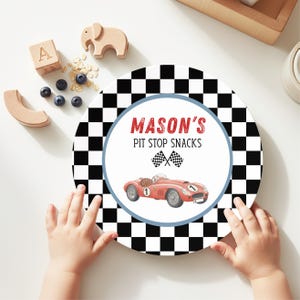 May include: A round plate with a black and white checkered border. The center features a red vintage race car, two crossed checkered flags, and the text MASON'S PIT STOP SNACKS in red and black lettering, all enclosed by a light blue circular border.