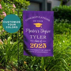 May include: A purple graduation garden flag with gold text that reads "Congratulations on your Master's Degree" and the graduate's name, class year, and university. A teal circle says "Customize Your Colors".