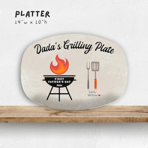 May include: Oval platter with the text "Dada's Grilling Plate". The design includes a grill, flame, and utensils. The platter is 14 inches wide and 10 inches high, with the text "First Father's Day 2026" and "Love, Willow".