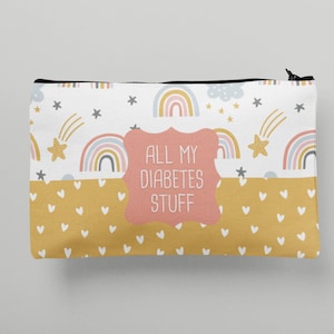 May include: A white zippered pouch with a pink and yellow rainbow pattern and gold stars. The pouch has a pink label that says "All My Diabetes Stuff".