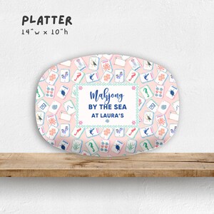 May include: Oval platter with a pink background and a pattern of Mahjong tiles. The platter is 14 inches wide and 10 inches high. The text "Mahjong by the Sea at Laura's" is in the center.