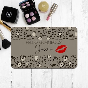 May include: A gray and black leopard print makeup bag with the text "Hello Gorgeous! Jessica" and a red lip print.