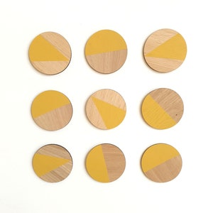 May include: Nine round wooden coasters with a yellow and natural wood geometric design.