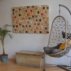 May include: A hanging chair with a grey cushion and a yellow pillow, a wooden chest, and a wall art piece made of colourful wooden squares.