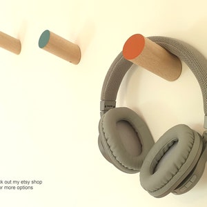 May include: Three wooden wall hooks with different coloured tops: yellow, teal, and orange. A pair of grey headphones are hanging on the orange hook.