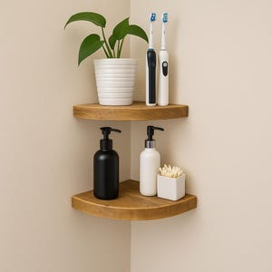 May include: Two wooden corner shelves with bathroom accessories. The top shelf holds a potted plant and two electric toothbrushes. The bottom shelf displays a black soap dispenser, a white soap dispenser, and a small white square container with cotton buds.