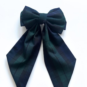 May include: A large green and black plaid bow with long tails. The bow is tied in a knot and the tails are pointed.