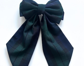 May include: A large green and black plaid bow with long tails. The bow is tied in a knot and the tails are pointed.