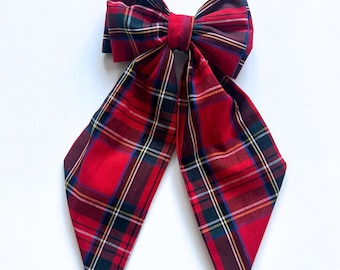 May include: A red and black plaid bow with long tails. The bow is tied in a classic shape and the tails are pointed.