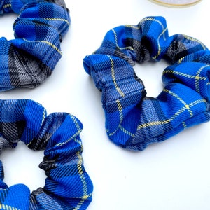 May include: Three blue and gray plaid scrunchies with yellow accents. The scrunchies are made of fabric and are tied together in a knot.