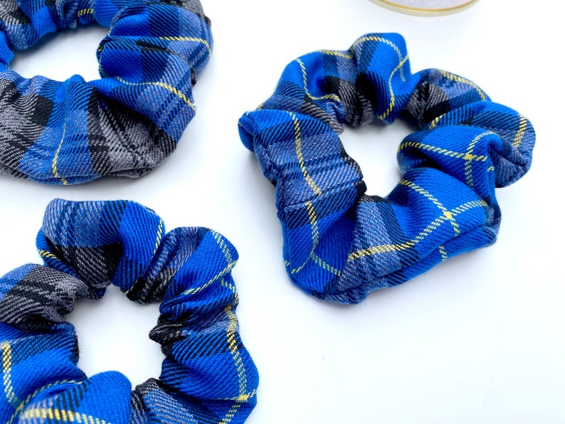 May include: Three blue and gray plaid scrunchies with yellow accents. The scrunchies are made of fabric and are tied together in a knot.