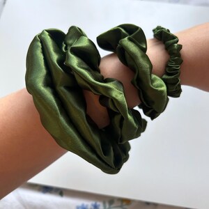 May include: Three green satin scrunchies, one large and two smaller, on a person's arm.