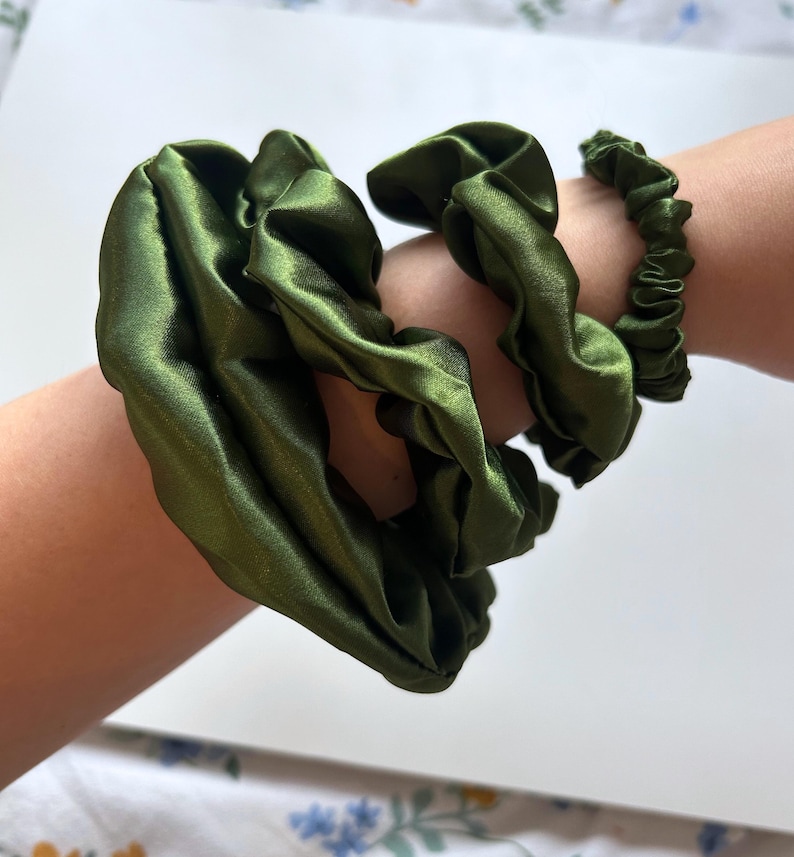 May include: Three green satin scrunchies, one large and two smaller, on a person's arm.