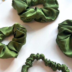 May include: Four green satin scrunchies of different sizes. The scrunchies are made of soft, silky fabric and are perfect for holding hair in place.