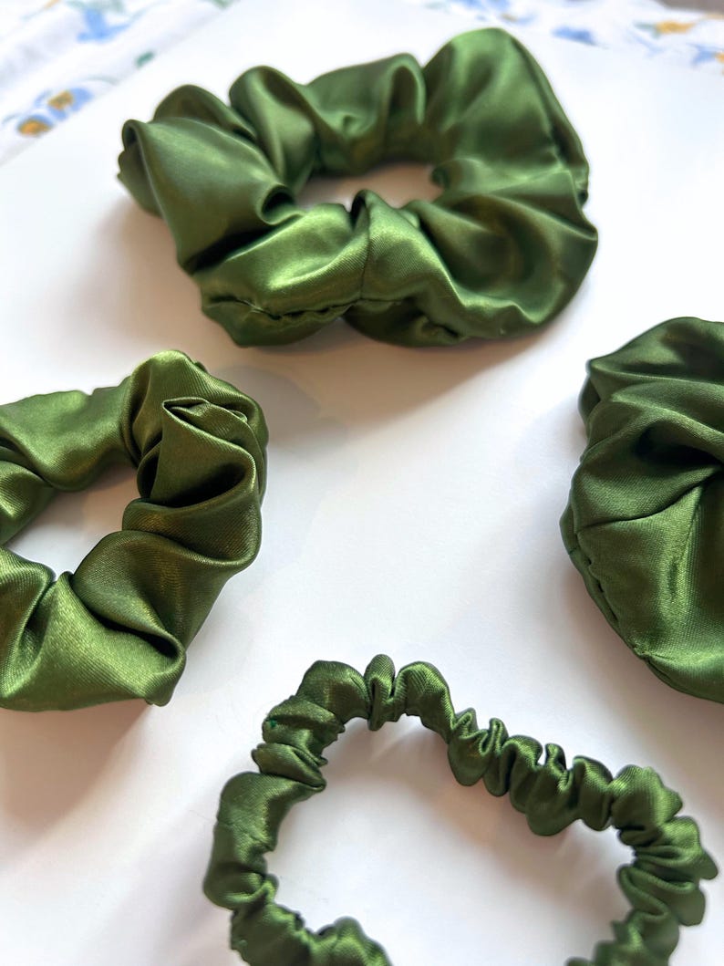 May include: Four green satin scrunchies of different sizes. The scrunchies are made of soft, silky fabric and are perfect for holding hair in place.