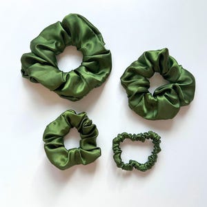 May include: Four green satin scrunchies of different sizes. The scrunchies are made of soft, silky fabric and are perfect for holding hair in place.