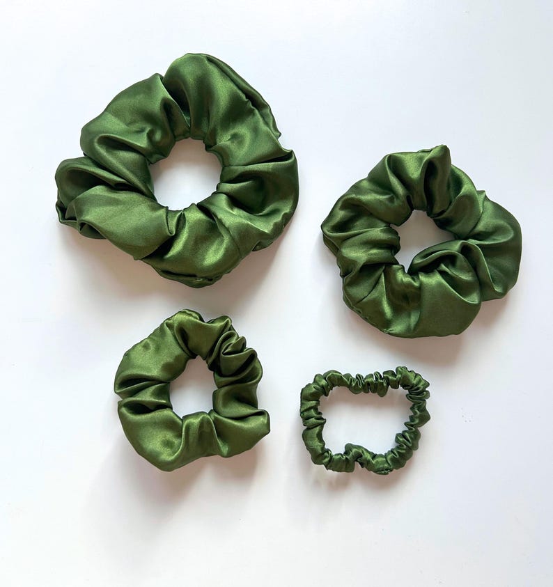 May include: Four green satin scrunchies of different sizes. The scrunchies are made of soft, silky fabric and are perfect for holding hair in place.