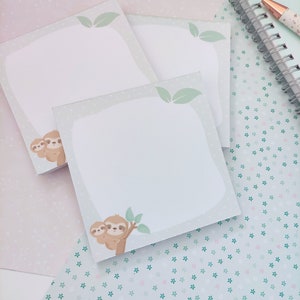 Könnte beinhalten: Drei pastellgrüne Haftnotizblöcke mit einem Faultier-Design. Jeder Block hat einen weißen Hintergrund mit einem grünen Rand und einer Faultier-Illustration. Das Faultier ist braun mit einem hellbraunen Bauch und hält ein grünes Blatt. Der Hintergrund des Bildes ist hellrosa mit einem weißen und grünen Muster.