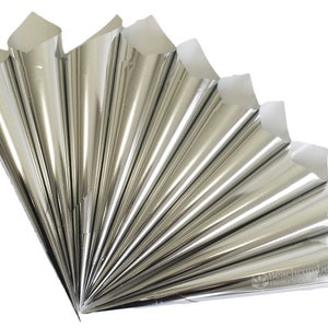 Könnte beinhalten: Fächerförmige Anordnung silberner Metallkegel, wahrscheinlich für Henna-Anwendungen. Die Kegel sind ordentlich gefaltet und angeordnet, mit weißen Papierspitzen. Das Bild ist gut beleuchtet und hebt die reflektierende Oberfläche der Kegel hervor. Der Text "Beachcombers Henna Supply & Studio" ist sichtbar.