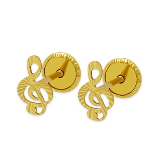May include: A pair of gold-colored stud earrings. Each earring features a stylized treble clef design. The earrings have a textured, ridged backing and a post for insertion. The earrings are set against a white background.