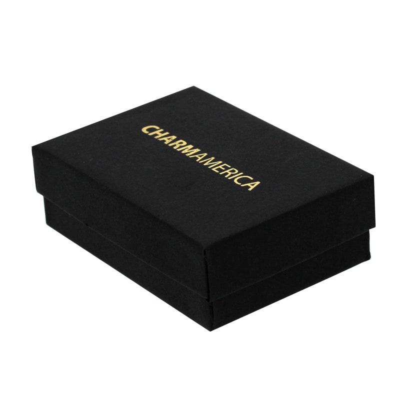K&ouml;nnte beinhalten: Eine rechteckige schwarze Geschenkbox mit Deckel. Auf der Oberseite der Box befindet sich das Wort CHARMAMERICA, das in goldenen Gro&szlig;buchstaben aufgedruckt ist. Die Box hat eine matte Oberfl&auml;che und ein strukturiertes Design zur Aufbewahrung.