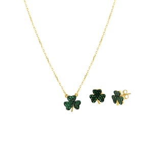 Op de afbeelding: Een goudkleurige sieradenset met een ketting en oorknopjes. Elk stuk heeft een klaverbladontwerp, bezet met groene edelstenen. De ketting heeft een fijne ketting en de oorbellen hebben push-backs.