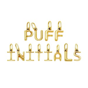 Op de afbeelding: Gouden initiaalbedels met het woord "PUFF INITIALS". Elke letter heeft een lus aan de bovenkant om aan een ketting of armband te bevestigen. De letters zijn in een vetgedrukte, schreefloze lettertype.