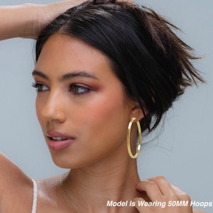 May include: A model wearing gold hoop earrings. The earrings are 50mm in diameter. Model Is Wearing 50MM Hoops