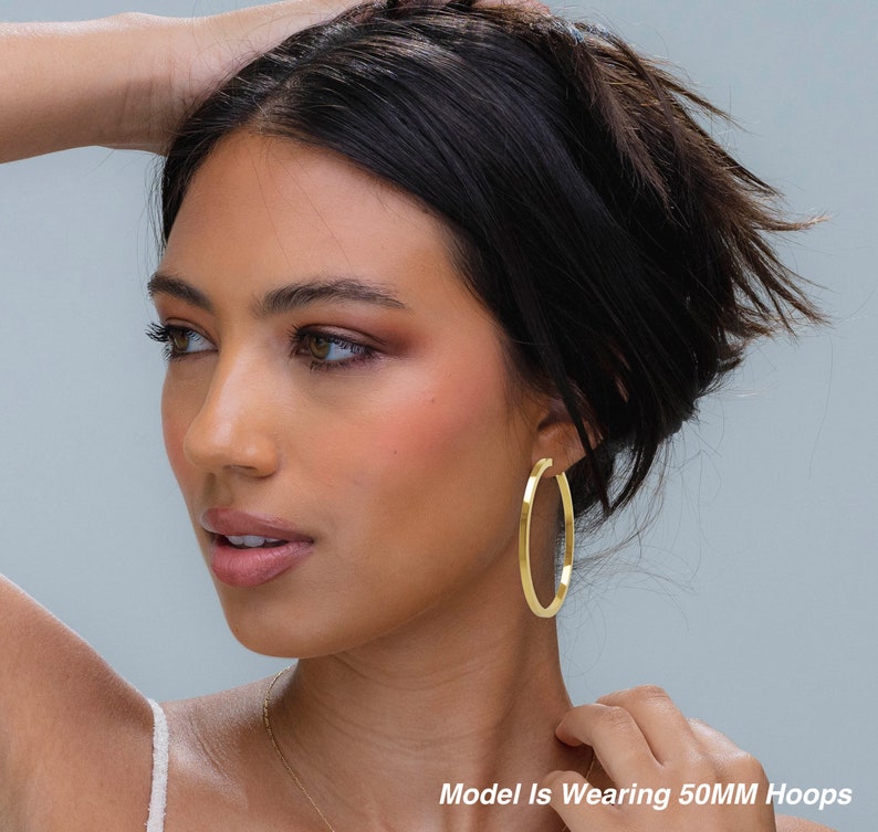 May include: A model wearing gold hoop earrings. The earrings are 50mm in diameter. Model Is Wearing 50MM Hoops