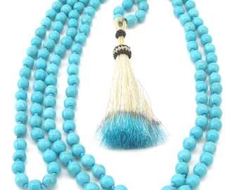 May include: A turquoise blue mala necklace with a white and blue horsehair tassel. The necklace is made of round beads and is approximately 18 inches long.