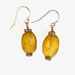 Peut inclure: Une paire de boucles d'oreilles dorées avec des pierres précieuses jaune-vert ovales et facettées. Les boucles d'oreilles ont des crochets d'oreilles dorés et des capuchons décoratifs dorés.