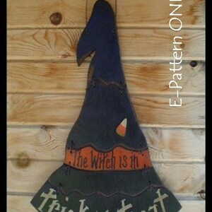 May include: A wooden witch's hat with a black and green paint scheme. The hat has a candy corn design and the text "The Witch is in... trick or treat" on the brim.
