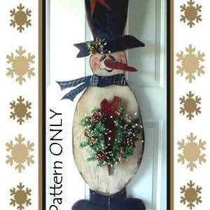 May include: A wooden snowman door hanger with a black top hat, a red star, a blue and white scarf, and a green wreath with pine cones. The snowman is painted white with a red nose and black eyes. The text "E-Pattern ONLY" is written vertically on the left side of the snowman.